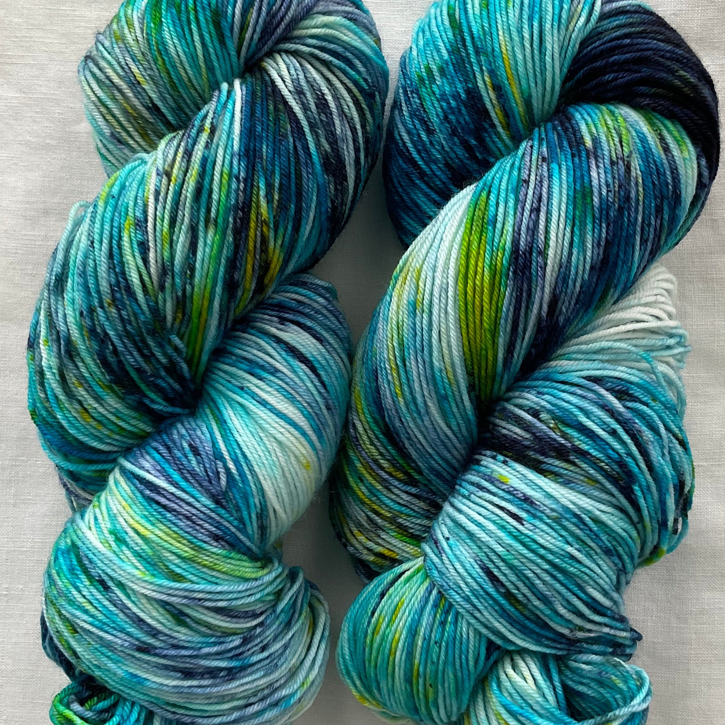 Two skeins of blue and green yarn on a white fabric background
