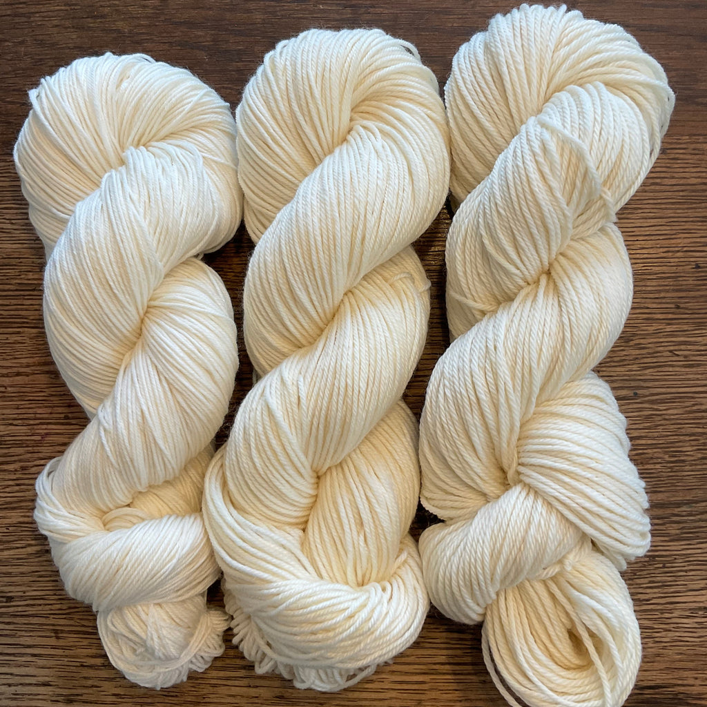 Three skeins of white yarn on a wooden surface