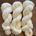 Three skeins of white yarn on a wooden surface
