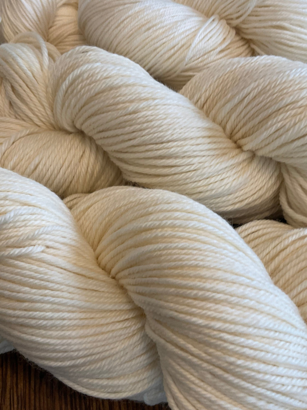 Three skeins of cream-colored yarn on a wooden surface